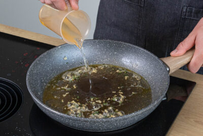 Weißwein und Brühe in die Pfanne gießen