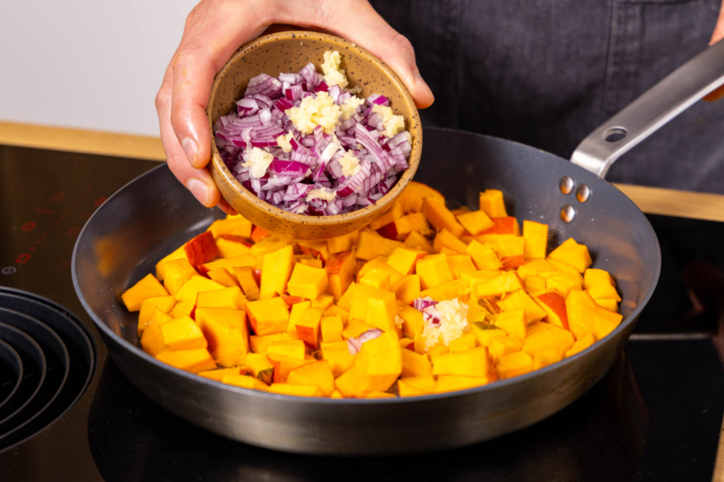 Zwiebel und Knoblauch zum Kürbis in die Pfanne geben