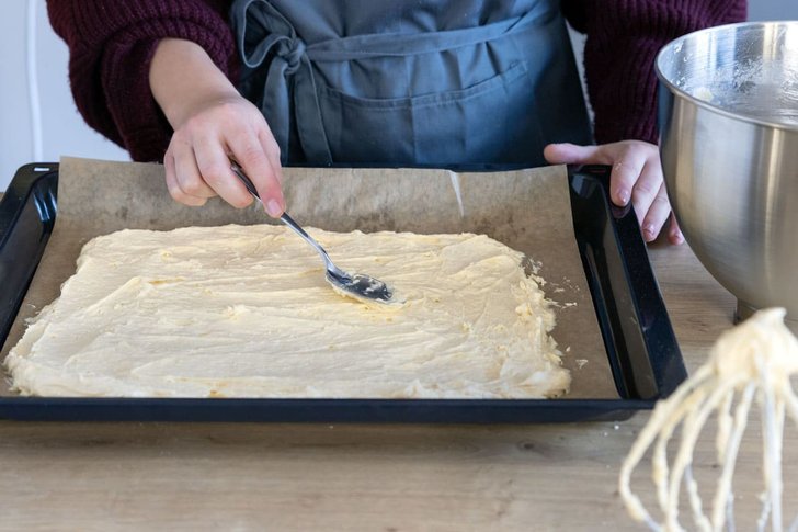 Erste Schicht Teig des Schneewittchenkuchens auf dem Blech verteilen