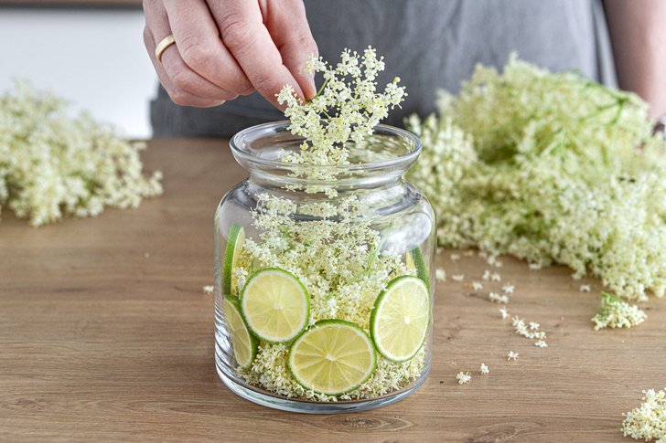 Holunderblüten und Limetten in ein Gefäß geben