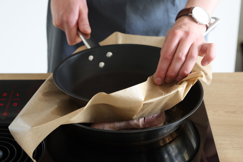 Mit Backpapier unterlegt Pfanne zum Anbraten auf Entenbrust drücken