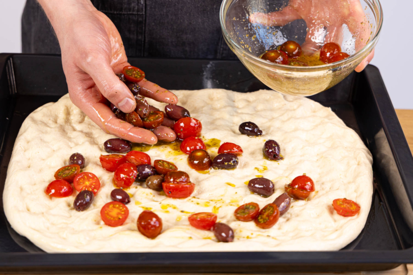marinierte Tomaten und oliven auf der Teig verteilen