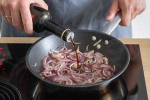 Balsamico-Essig zu den karamellisierten Zwiebeln hinzugeben