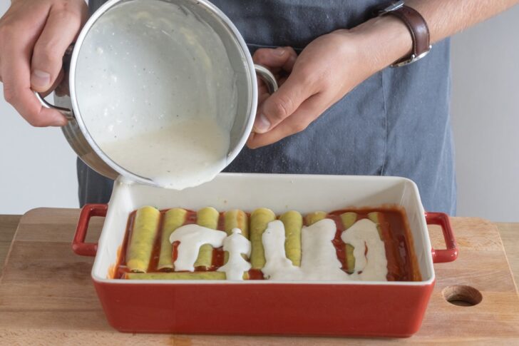 Bechamelsauce über die Cannelloni mit Spinat und Ricotta geben