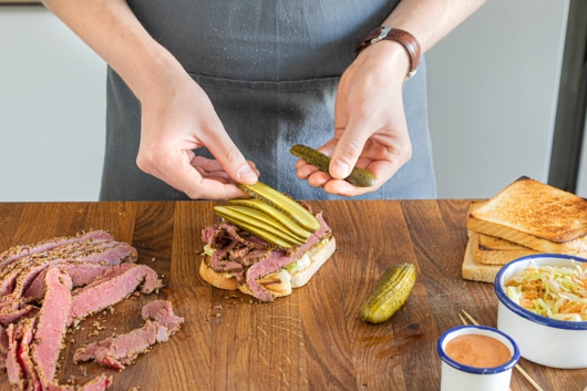 Gewürzgurken auf das Sandwich legen