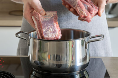 Rindfleisch mit Knochen in den Topf geben