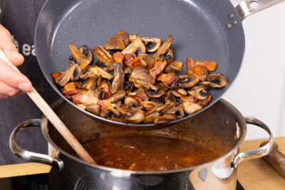 Pilze und Speck mit in die Soße geben.