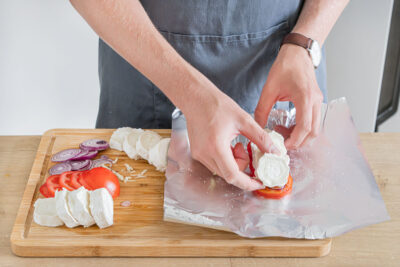 Tomate, Zwiebeln, Knoblauch und Käse auf der Alufolie verteilen