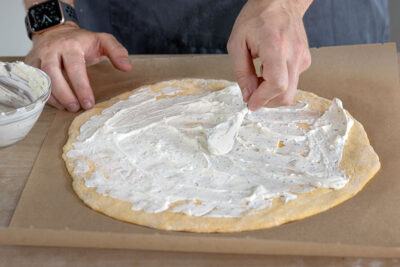 Crème fraîche auf der Pizza verteilen