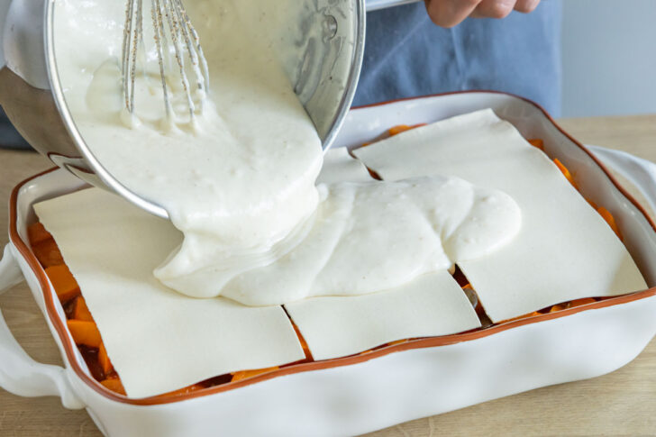Bechamelsauce über Kürbislasagne geben