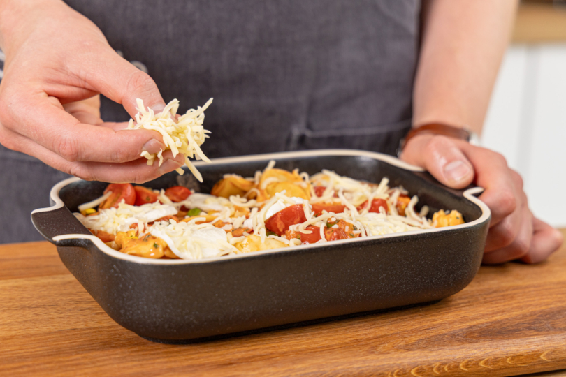 Käse auf dem Tortellini Auflauf verteilen