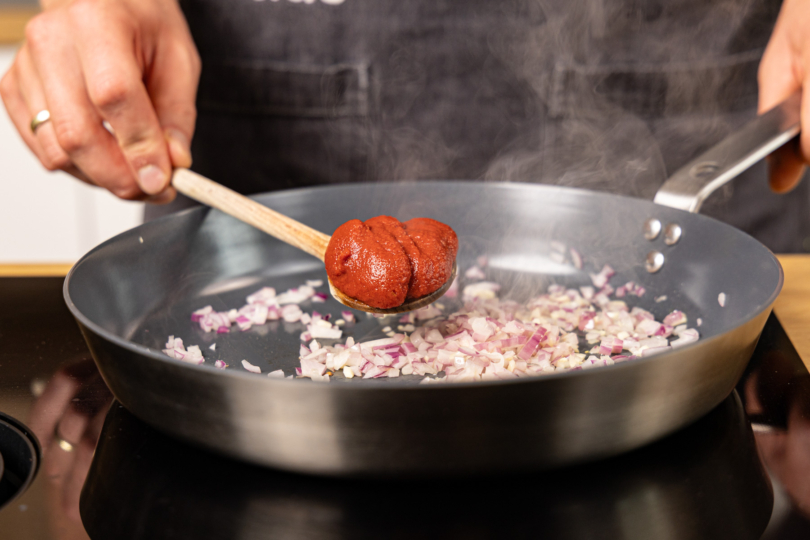 Tomatenmark in die Pfanne geben