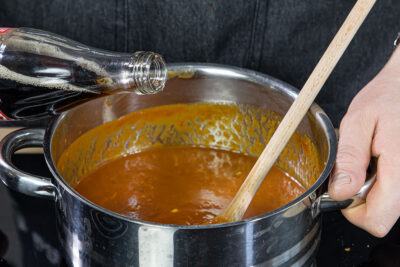 passierte Tomaten, Orangensaft und Cola zur Currywurst-Sauce geben