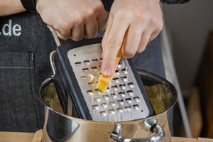 Käse für das Käsefondue in den Topf reiben