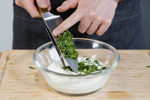 Kräuter zu dem Joghurt geben, um den Dip für die Köfte Spieße herzustellen.
