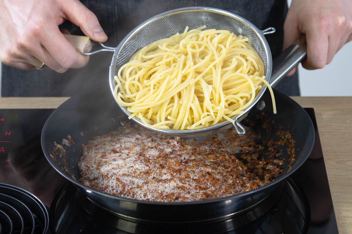 Die Spaghetti in die Pfanne dazugeben.