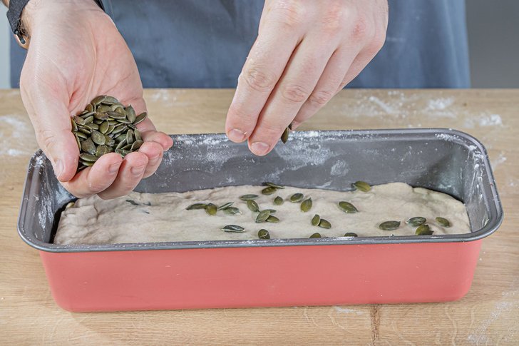 Teig in die Form geben und mit Kürbiskernen bestreuen