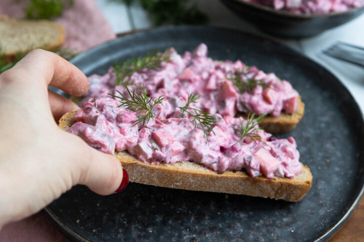 Den roten Heringssalat mit roter Bete auf einer Scheibe Brot servieren.