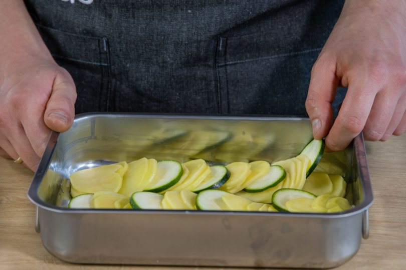 Zucchini und Kartoffeln in eine Auflaufform schichten
