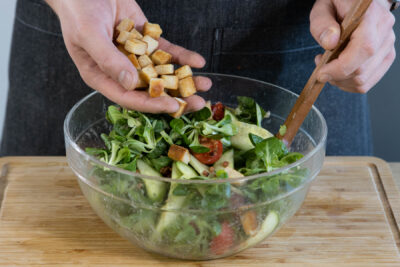Croutons in den Feldsalat mit Speck geben.