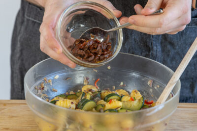 Getrocknete Tomaten in den Gnocchi-Salat geben