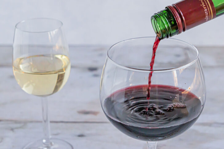 Rotwein wird in Glas eingegossen, im Hintergrund ein Glas Weißwein