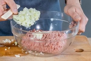 Zwiebel und Knoblauch zum Hackfleisch geben
