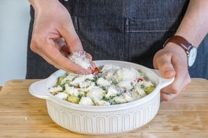 Grana Padano über Gnocchi-Spinat-Auflauf streuen