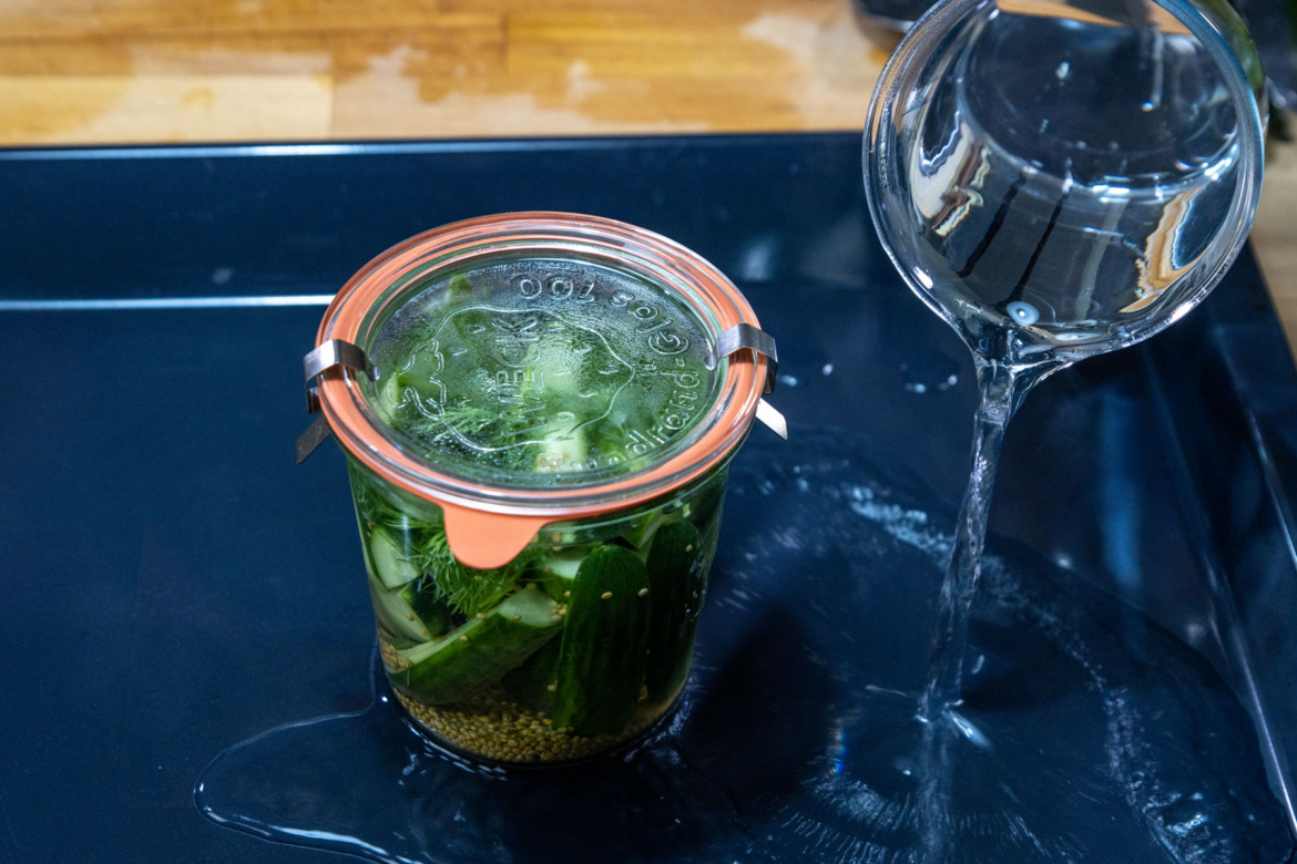 Gefülltes Gurkenglas auf ein Backblech stellen, Wasser zugeben und alles in den Ofen geben.