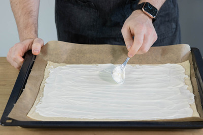 Flammkuchen mit Schmand bestreichen