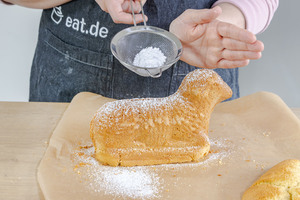 fertig gebackenes saftiges Osterlämmchen aus Rührteig mit Puderzucker bestreuen