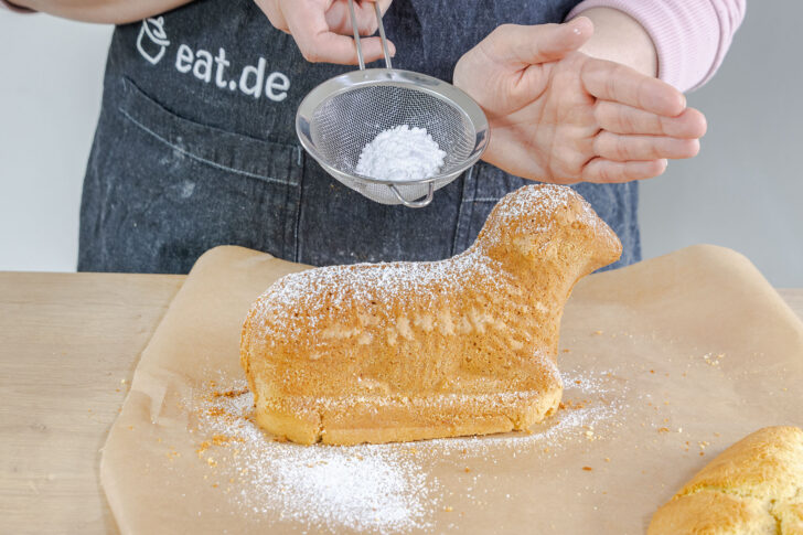 fertig gebackenes saftiges Osterlämmchen aus Rührteig mit Puderzucker bestreuen
