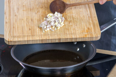 Zwiebel und Knoblauch in die Pfanne geben