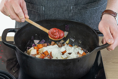 Tomatenmark und Mehl zum Gemüse geben