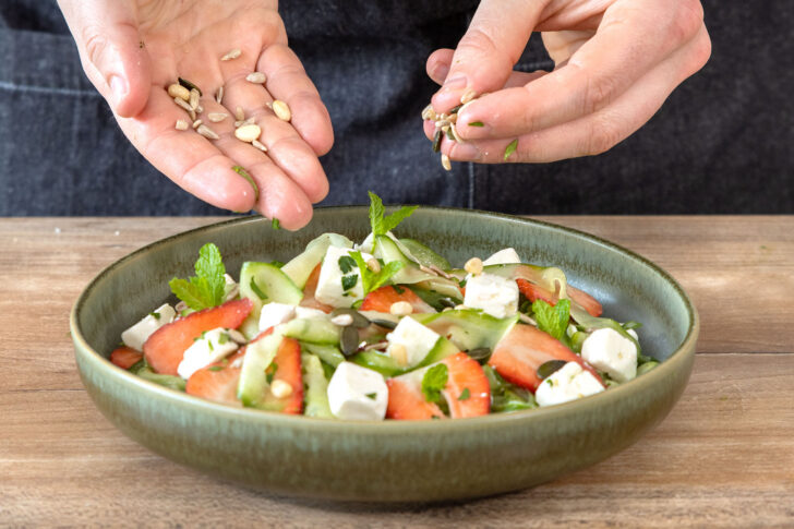 Sonnenblumenkerne über den Gurkensalat mit Erdbeeren und Feta geben