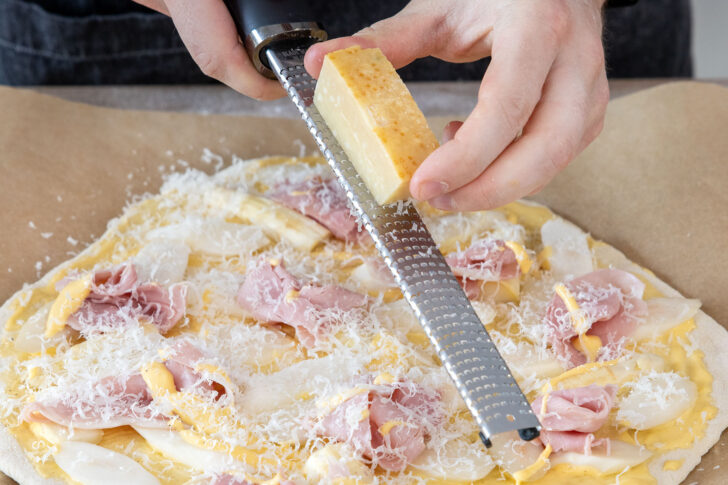 Parmesan über Spargelpizza mit Schinken und Sauce Hollandaise reiben