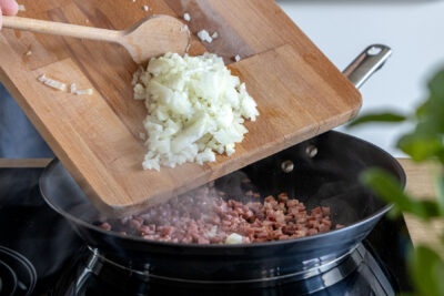 Zwiebel zu gebratenen Schinkenwürfeln geben