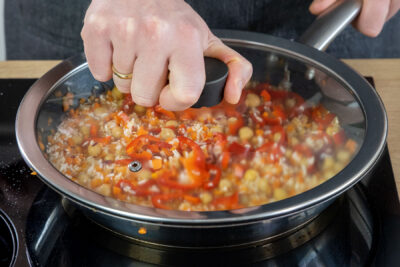 Vegane Gemüsepfanne mit Reis abgedeckt köcheln lassen