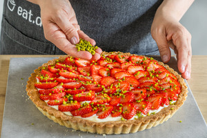 Pistazien über den Erdbeerkuchen mit Vanillecreme geben