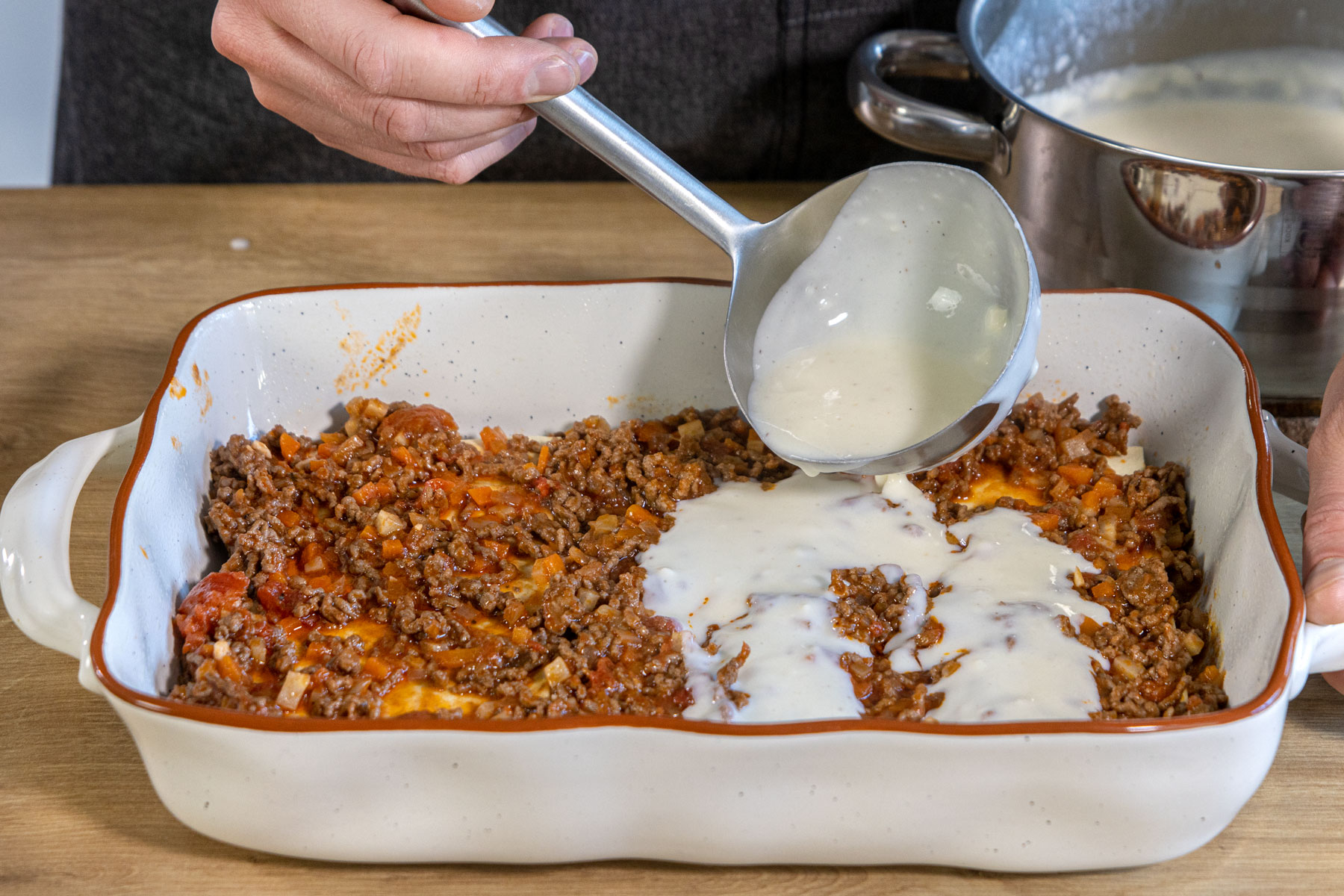 Béchamelsaucen auf der Bolognese-Lasagne verteilen