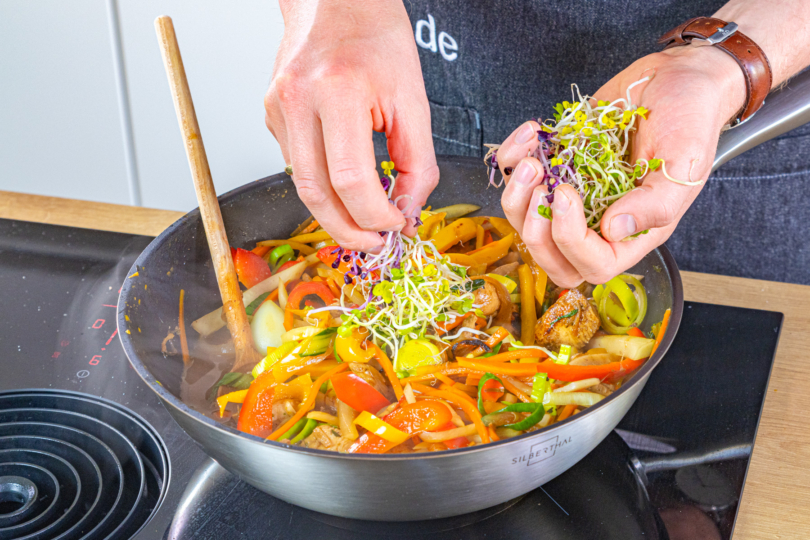 asiatische Wokpfanne mit Sprossen garnieren
