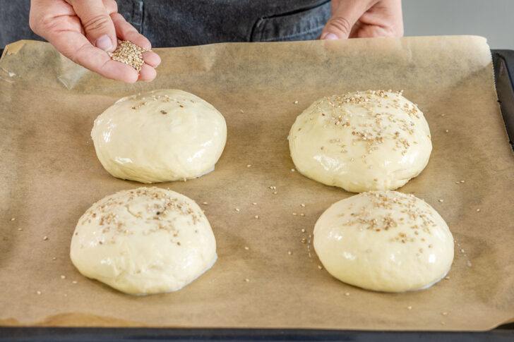 Vegane Burger Buns mit Sesam bestreuen