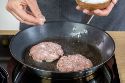 Wildschwein Burger Patties in der Pfanne salzen