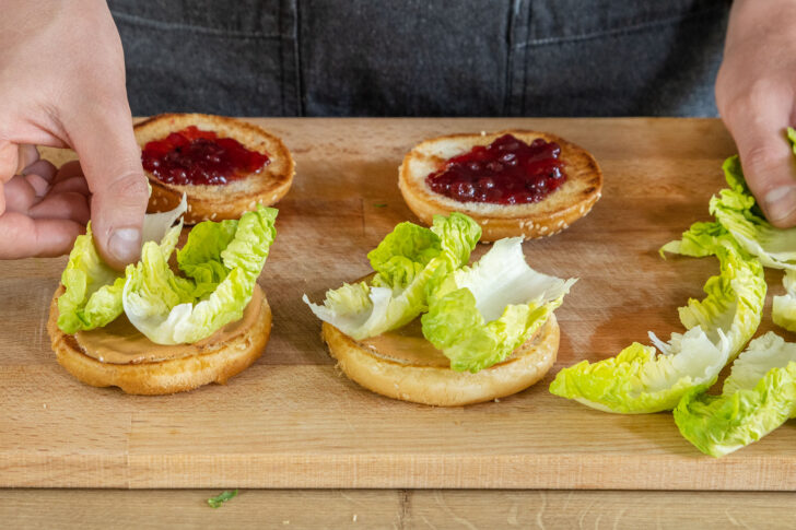 Bürgerbrötchen mit Dressing und Preiselbeeren bestreichen und Romanasalatblätter darauflegen