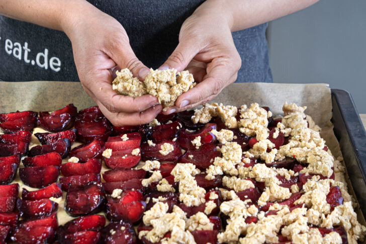 Streusel auf dem Pflaumenkuchen mit Pudding verteilen