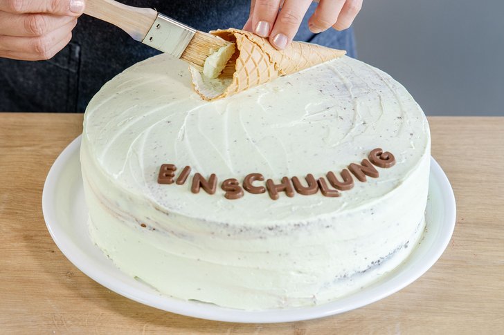 Eiswaffel auf der Torte zum Schulanfang platzieren und ihnen mit etwas Buttercreme bestreichen