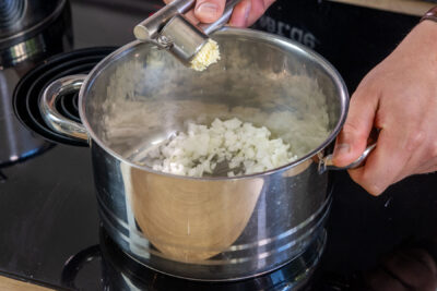 Knoblauch zur Zwiebel in den Topf pressen
