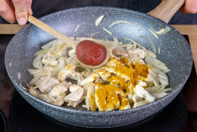 Curry und Tomatenmark zu dem Fleisch geben