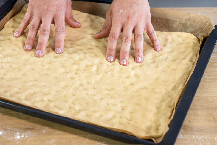 Luftblasen mit den Fingern aus dem Boden für den klassischen Zwetschgenkuchen mit Streusel drücken
