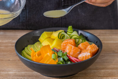 Vinaigrette über Poké-Bowl geben